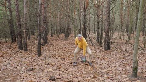 Man lifting kettlebell overhead during outdoor fitness session in forest Video stock 324556937