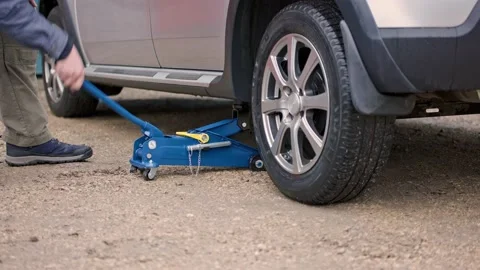 Man lifting up silver car with blue hudraulic floor car jack Stock Footage 164504973