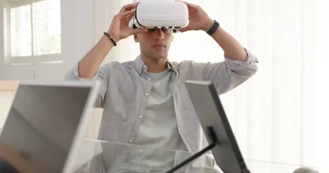 Man lifting white VR headset off glass desk home office, fitting over eyes 스톡 동영상 335781159