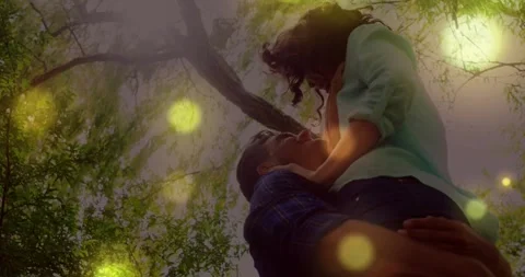 Man lifting woman under tree, eye contact sparking embrace, golden bokeh Stock Footage 331235227