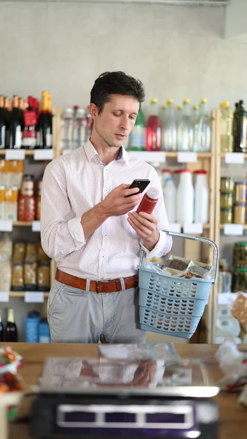 Man in light shirt scan QR code and take reading red smoothie label using phone Stock Footage 327697210