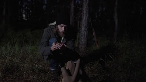 Man lighting a campfire in a forest at night. Blowing fire on his hand. Stock Footage 76409090