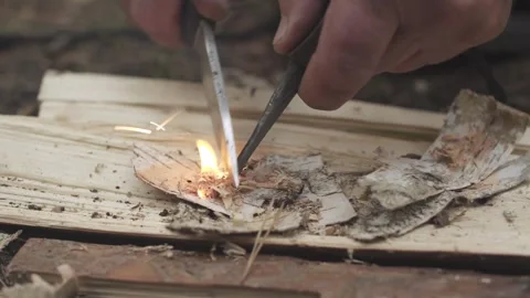 Man lighting fire tinder from birch bark using flint and steel in the forest. Video stock 280227152