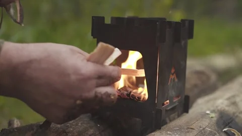 Man lighting fire using wood chips in portable folding wood stove in the forest. Video stock 280227107