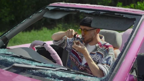 Man lights and smokes weed from pipe, sitting in pink cabriolet Stock Footage 233897642