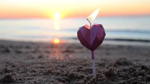 A man lights a candle in the shape of heart on sea sandy beach at dawn sunset. Stock Footage 212842878