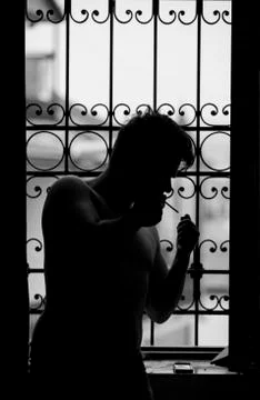 A man lights a cigarette while sitting on a windowsill Stock Photos