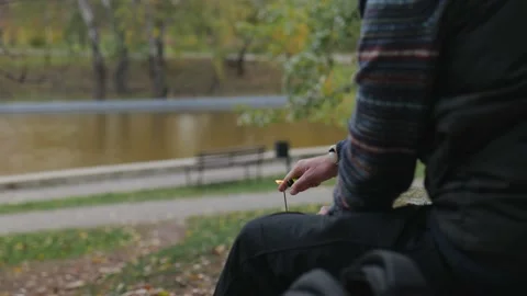 A man lights an incense stick with a lighter against the backdrop of a pond Stock Footage 229860344