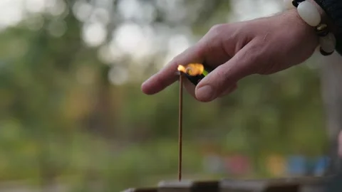 A man lights an incense stick with a lighter against a blurred background Stock Footage 229860407
