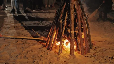 A man lights a large bonfire on a sandy beach. A burning bonfire on the beach Stock Footage 310249153