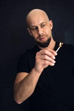 Man lights a match while looking closely at the flame in a dark setting Stock Photos