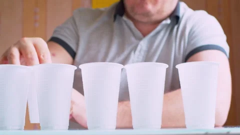 Man lining up plastic cups on a table. Blurred silhouette in a bright room Stock Footage 336202650