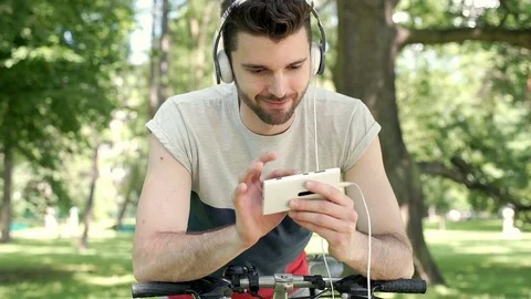 Man listening music and browsing internet on smartphone while leaning on his bik Stock Footage