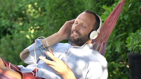Man listening to music and singing lying on hammock in garden, super slow motion Stock Footage