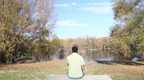 Man listening to music using headphones while sitting by lake Stock Footage 59554669