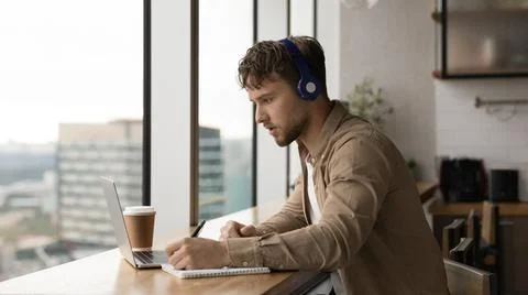 Man listens audio taking notes making assignment use laptop Foto stock