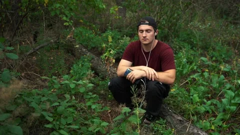 A man listens to music while sitting on a felled tree in the forest Stock Footage 165554233
