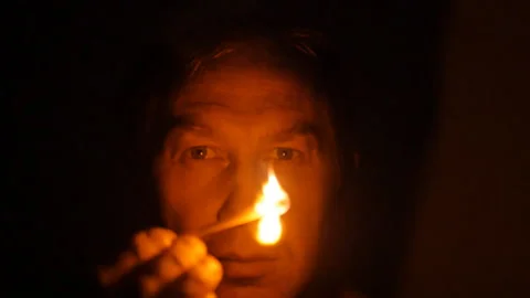 The man lit a match in the dark. The person's face is lit by fire from a match. Stock Footage 161896623