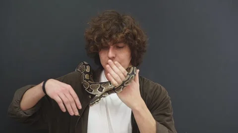 A man is a little afraid of a snake that crawls on his hand, a confused young Stock Footage 158143079