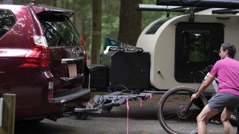 Man Loading Bicycles Onto Car at Campground With Teardrop Trailer Nearby Stock Footage 313899275