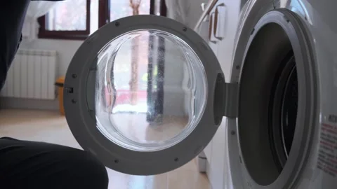 A man loading clothes into a front-loading washing machine in the laundry room 스톡 동영상 307742478