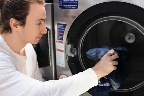 Man loading clothes into washing machine. Person doing laundry at self-serv.. Stock Photos