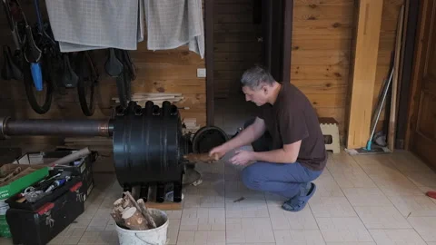 Man loading firewood into stove for heating in wooden house Stock Footage 335133686