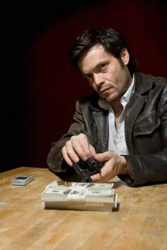 A man loading a gun with bullets next to several stacks of money Stock Photos