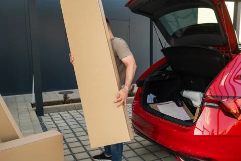 Man loading large cardboard boxes into hatchback vehicle at outdoor parking area Foto stock