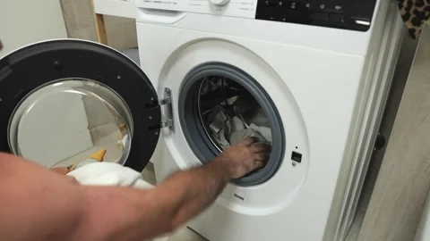 Man loading laundry into washing machine, demonstrating household chores and Stock-Footage 313725679
