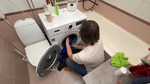 Man loading laundry into a washing machine in a bathroom, home hygiene routine Stock Footage 336981341
