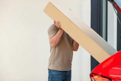 Man loading long cardboard box into trunk of red vehicle during home delivery Stock Photos