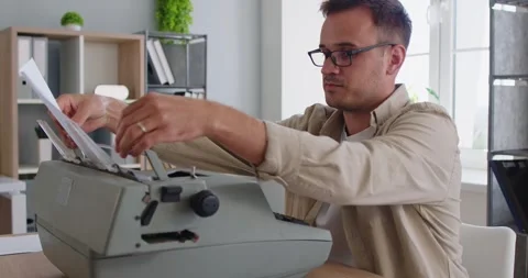 Man loading paper pages into vintage typewriter at desk in modern office Stock Footage 322996000