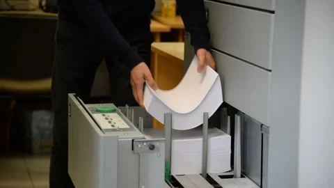 A man loads many blank paper sheets into the big printer's slot Stock Footage 102369118