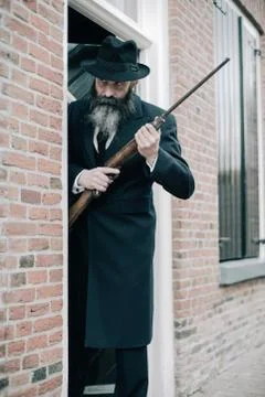 Man with long beard dark dressed standing with rifle ready to shoot. Stock Photos