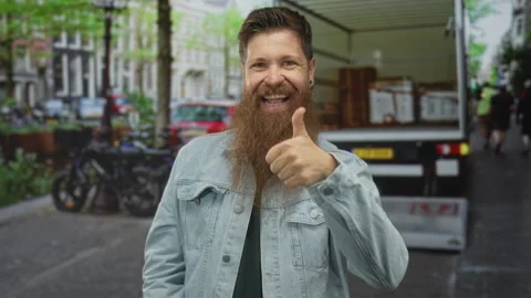 Man with long ginger beard gives thumbs up on bustling street beside delive.. Stock Footage 312792170