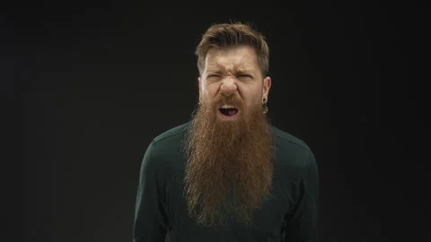 Man with long ginger beard grimacing with open mouth and furrowed brow in b.. Stock Footage 313024386
