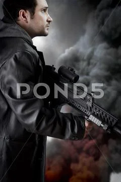 Man with long leather jacket and assault rifle, black smoke background Stock Photos