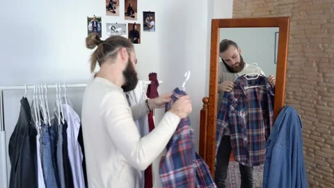 Man in a long sleeves  is looking in a mirror Talking on phone Choosing shirt Stock Footage 147892953
