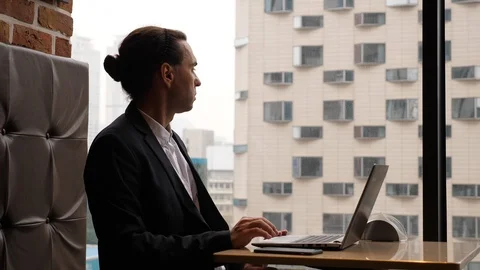 Man look out window, tap fingers, then pull oneself up and continue work Stock Footage 125017195