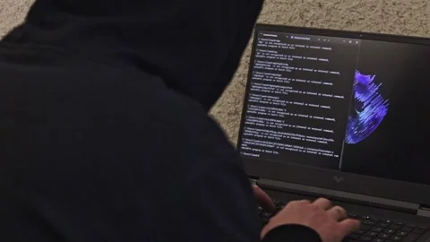 Man looked like hacker in a hood sitting in the front of laptop, writing a .. Stockbeeldmateriaal 259514045