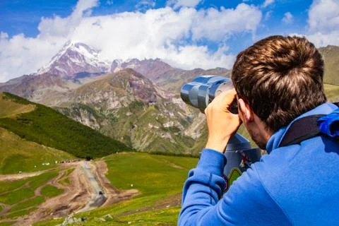 Man looking in binoscope directed towards the snowy mountain tops of Kazbeg f Stock Photos