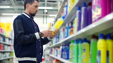 Man looking on bottle of washing detergent in the mall and reading the label Stock-Footage 76937964