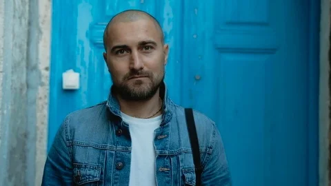 Man looking at the camera and smiling at the blue door background Stock Footage 82630517