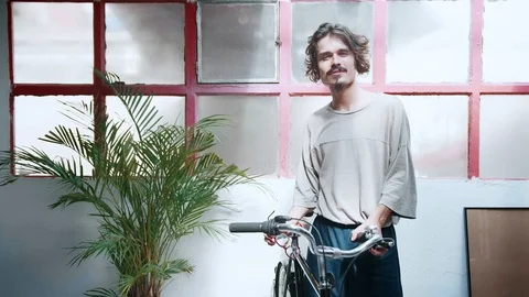 Man is looking to camera and smiling keeping old school bicycle in a bright loft Stock Footage 98895438