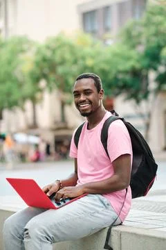 Man looking at camera and smiling while using a laptop outdoors. Stock Photos