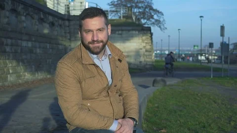 Man looking at camera sitting on wall at boulevard next to river  Vidéo 72775166