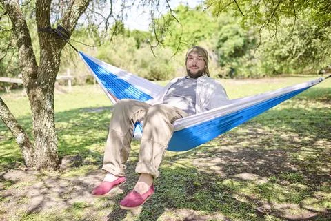 Man looking at the camera smiling while sitting in a hammock, resting outdoor Stock Photos