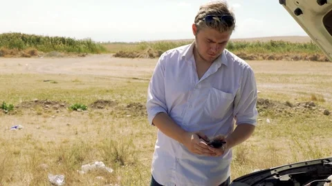 A man is looking at a device in his hands while the hood of his car is open. Stock Footage 319825335