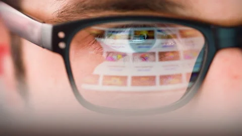 Man Looking at Device with Thumbnail Videos Reflected in his Eyeglasses. Stock Footage 167078413
